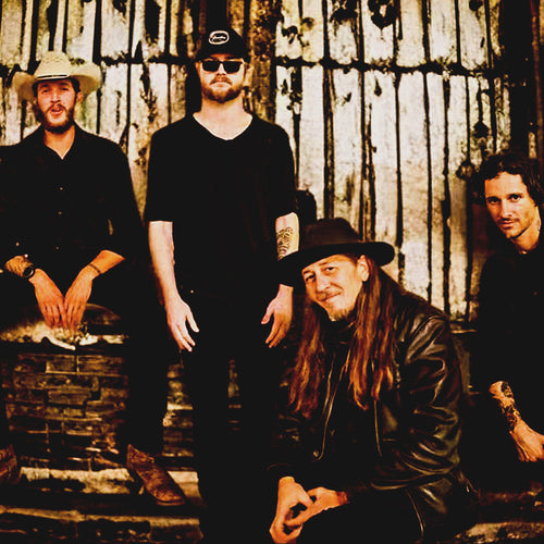 MNTN Goat ONE on Stage band image. Four people standing, kneeling, and sitting against brick distressed background.