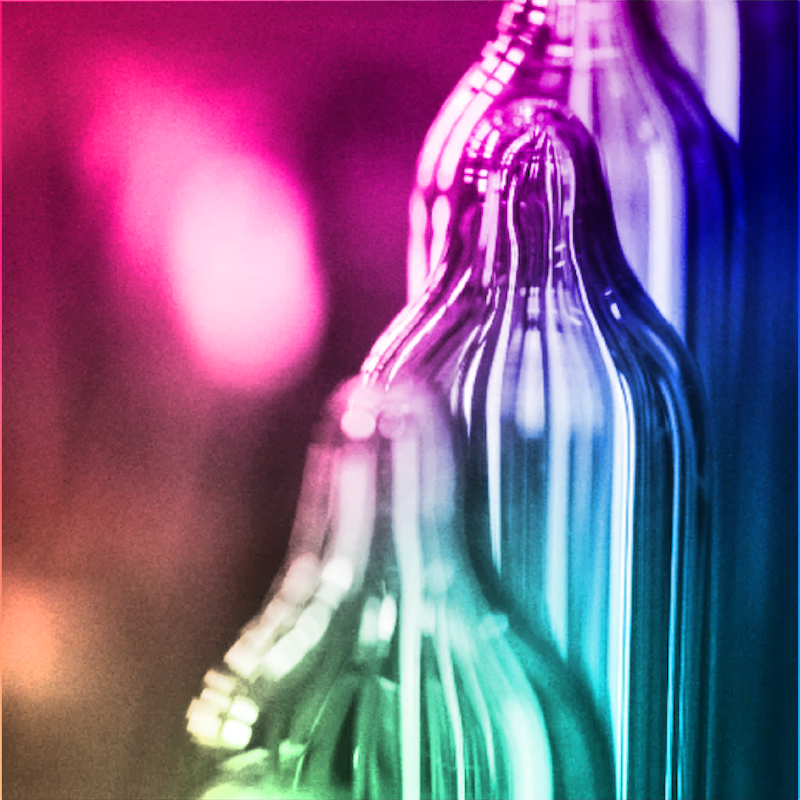 Three glass condom molds standing in a line with a colorful light reflection on them.