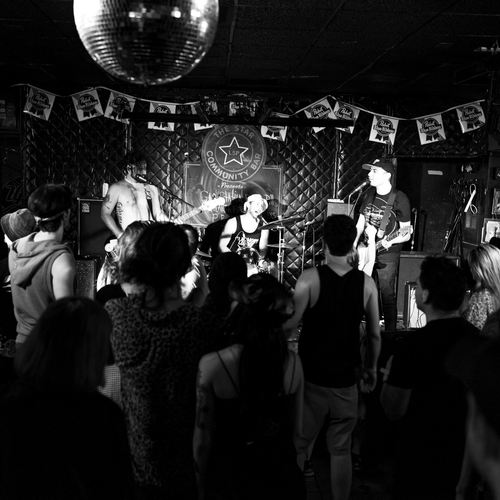 Live band performing on stage with a crowd in a bar setting.