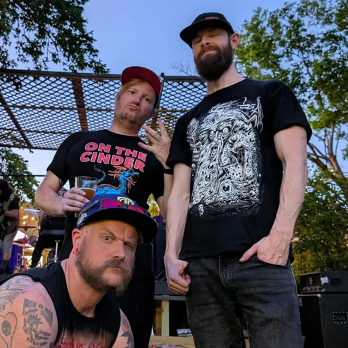Three men standing outdoors, two wearing black t-shirts with graphic designs, one holding a drink.