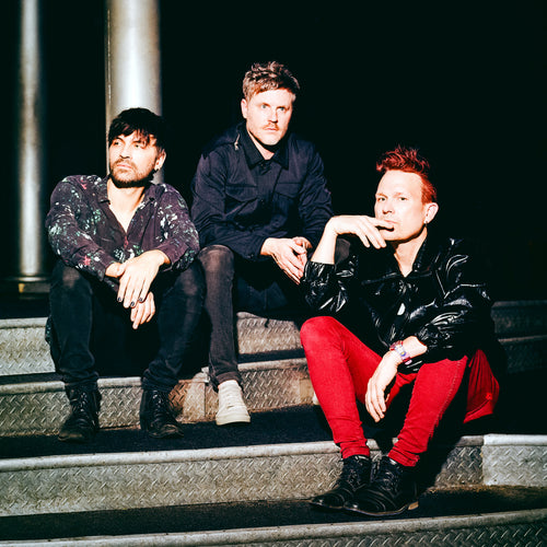 Night Drive - a ONE on Stage band. Three people sitting on stairs. 