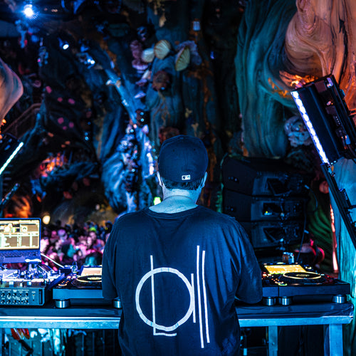 Image of person standing behind a DJ stand. Crowd in background. 