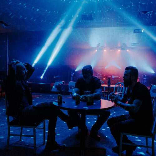 Image of Rebreather - a ONE on Stage band. Three people sit at table with a stage in the background. 
