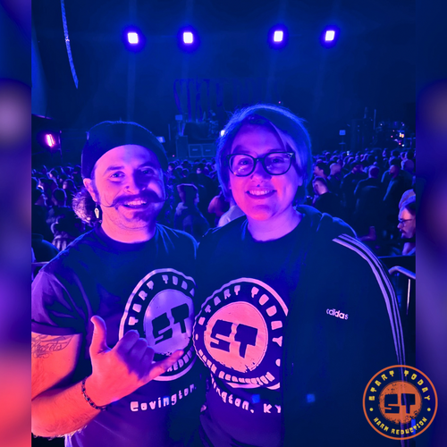 Two people at a concert with purple and blue lighting, wearing matching t-shirts.