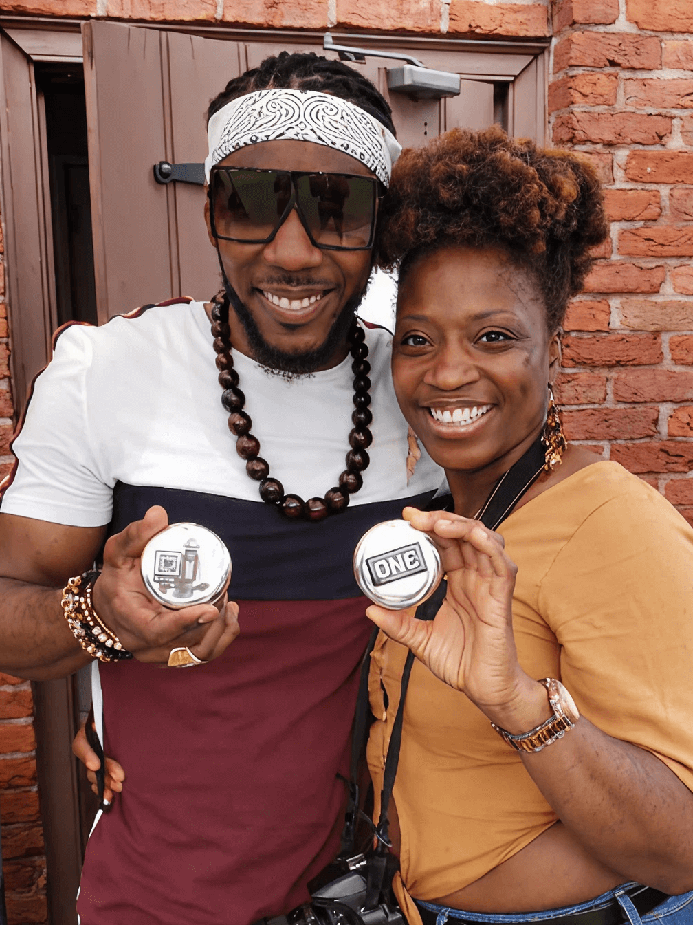 Two people holding two round objects with 'ONE' printed on them against a brick wall.