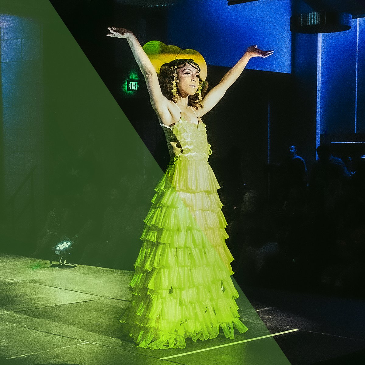 A person in a condom dress holding their arms in the air while on stage at a Project Condom event!
